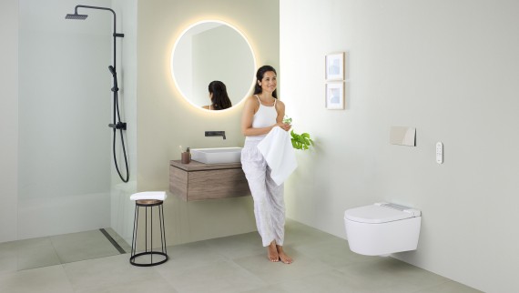 Femme appuyée sur un lavabo dans une salle de bains avec douche Geberit AquaClean Sela. Femme appuyée sur un lavabo dans une salle de bains avec douche Geberit AquaClean Sela.