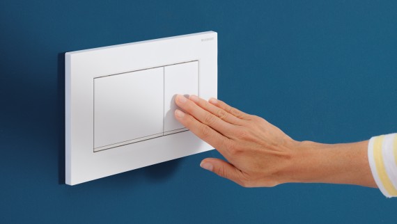 Main activant le rinçage sur une plaque de déclenchement noire Sigma50 (© Geberit)