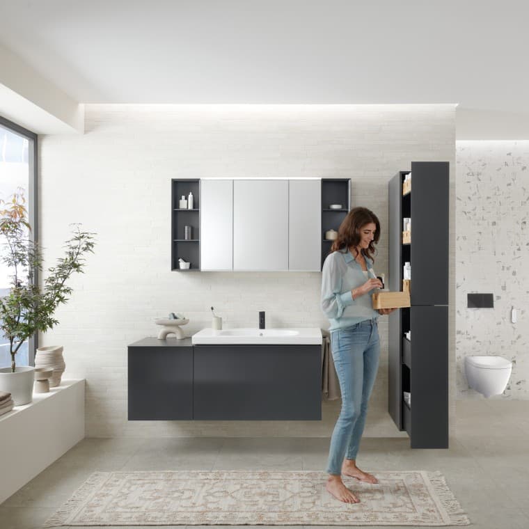Femme ouvrant une colonne haute avec beaucoup d‘espace de rangement dans une salle de bains avec meubles de salle de bains Geberit Acanto Femme ouvrant une colonne haute avec beaucoup d‘espace de rangement dans une salle de bains avec meubles de salle de bains Geberit Acanto