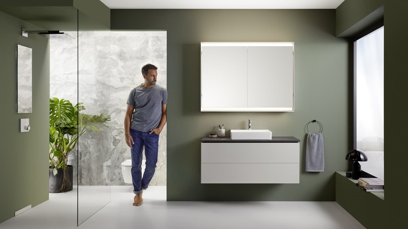 Homme debout dans une salle de bains présentant la série de salles de bains Geberit ONE Homme debout dans une salle de bains présentant la série de salles de bains Geberit ONE