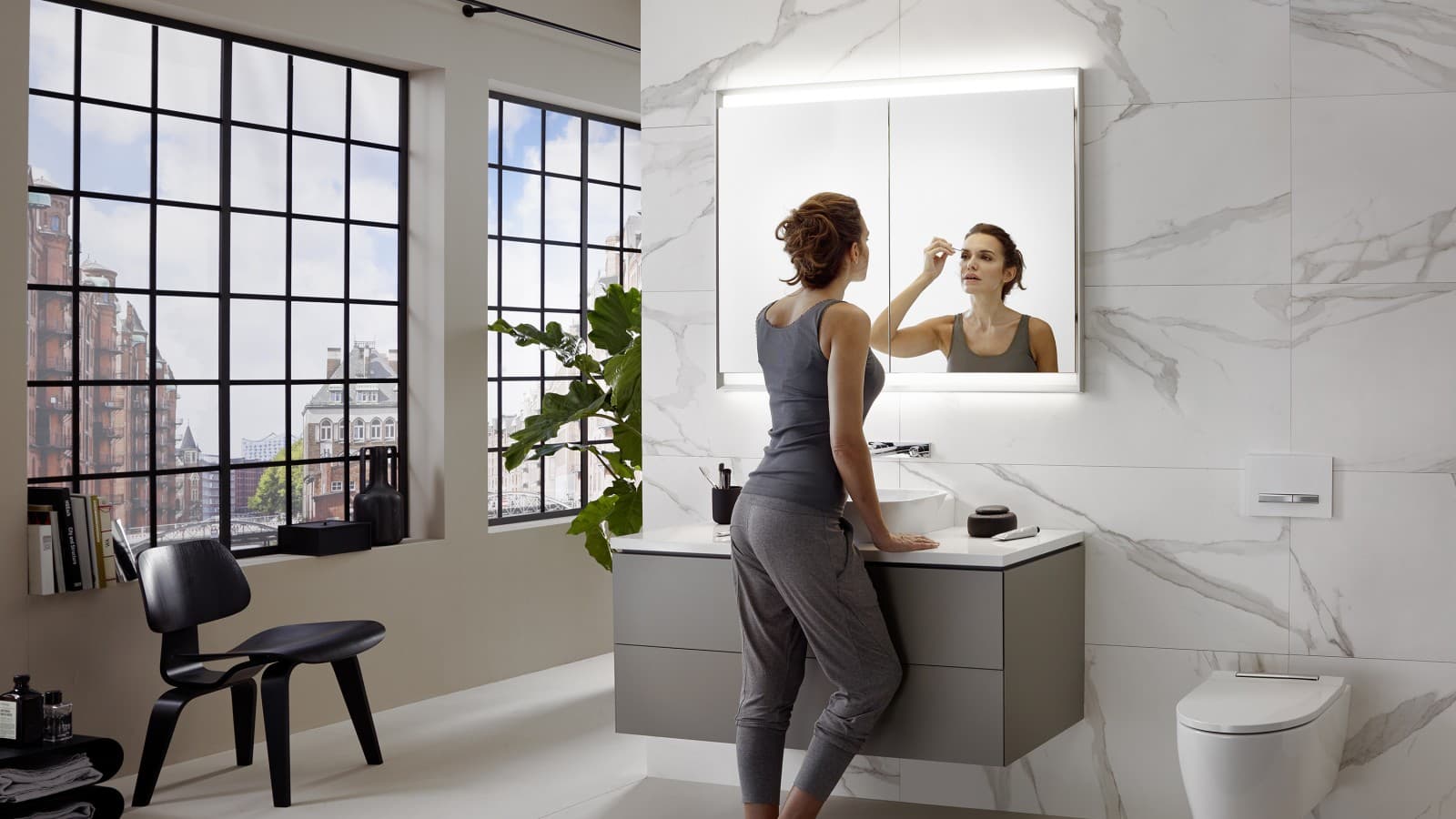 Une femme se tient dans une salle de bains Geberit ONE, où le lavabo est installé à la hauteur idéale. Une femme se tient dans une salle de bains Geberit ONE, où le lavabo est installé à la hauteur idéale.