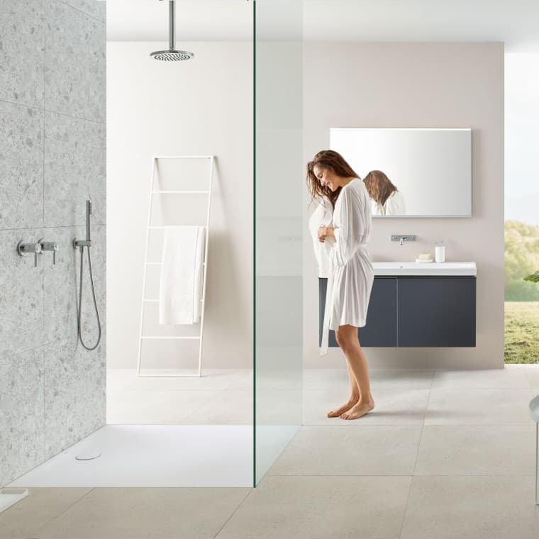 Femme dans une salle de bains avec douche walk-in et receveur de douche Geberit Olona Femme dans une salle de bains avec douche walk-in et receveur de douche Geberit Olona