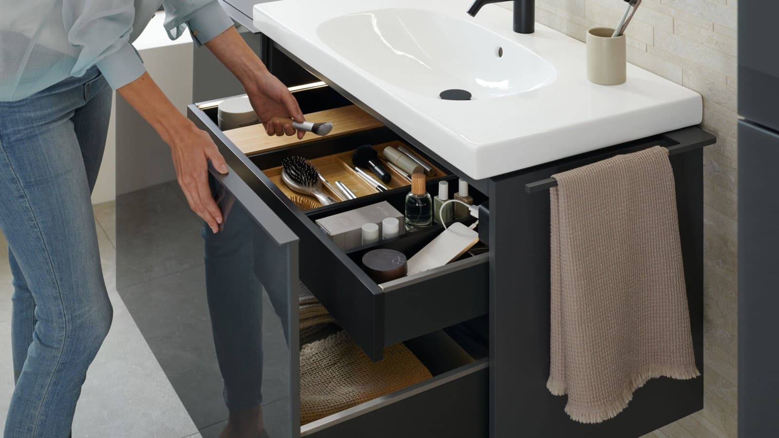 Une femme prend un pinceau dans le tiroir ouvert d’un lavabo Geberit Acanto dans le coloris gris velouté Une femme prend un pinceau dans le tiroir ouvert d’un lavabo Geberit Acanto dans le coloris gris velouté