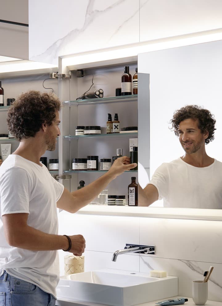 Homme dans une salle de bains avec armoire à mirroir Geberit One Homme dans une salle de bains avec armoire à mirroir Geberit One