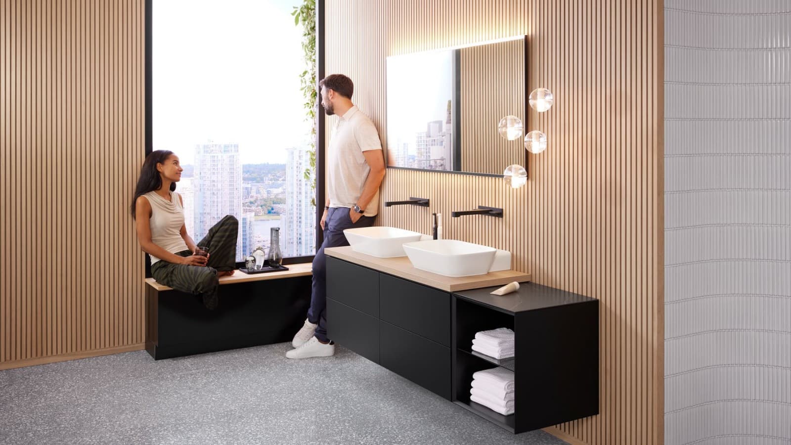 Une femme et un homme dans une grande salle de bains avec un double lavabo Geberit ONE, un miroir Option et des éléments en bois. Une femme et un homme dans une grande salle de bains avec un double lavabo Geberit ONE, un miroir Option et des éléments en bois.
