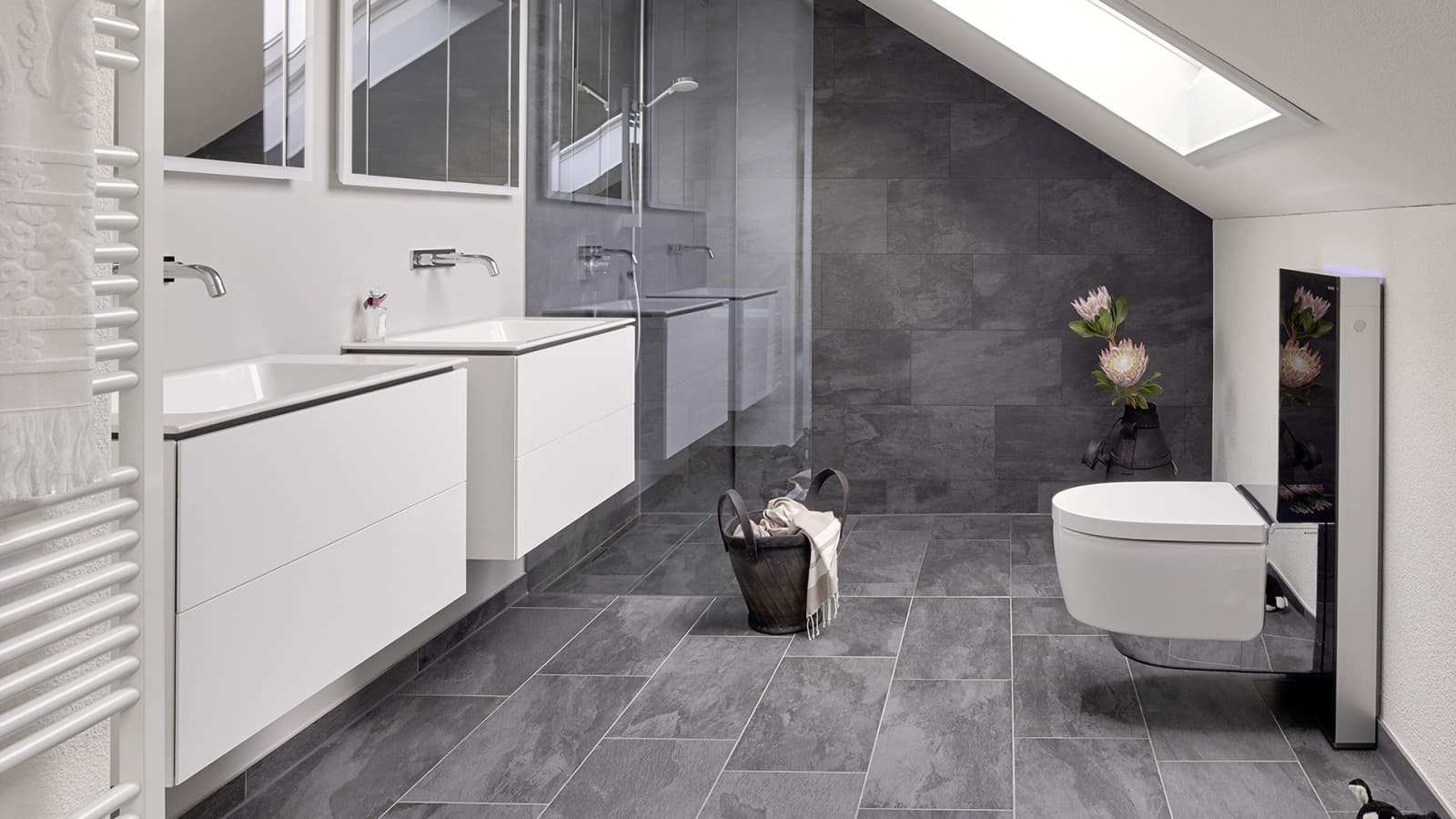 Salle de bains familiale sous toiture inclinée, aménagée avec des produits de la collection de salle de bains Geberit ONE, un WC-douche Geberit AquaClean Mera Comfort et le module sanitaire Geberit Monolith. Salle de bains familiale sous toiture inclinée, aménagée avec des produits de la collection de salle de bains Geberit ONE, un WC-douche Geberit AquaClean Mera Comfort et le module sanitaire Geberit Monolith.