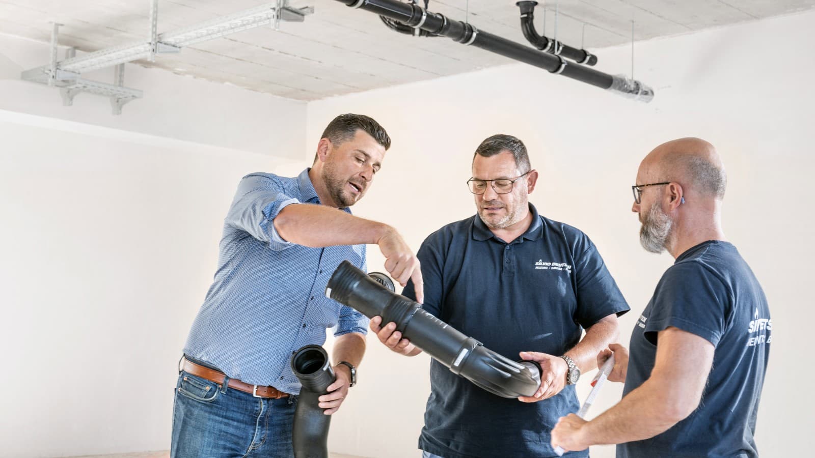 Fabian Ritter, conseiller commercial chez Geberit, présente le nouveau coude Geberit Silent-Pro BottomTurn au chef de projet Marcel Roth et à son équipe Fabian Ritter, conseiller commercial chez Geberit, présente le nouveau coude Geberit Silent-Pro BottomTurn au chef de projet Marcel Roth et à son équipe